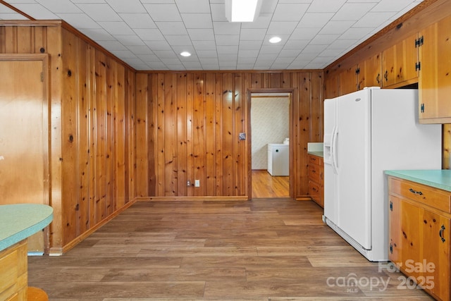 kitchen featuring washer / clothes dryer, wood walls, light hardwood / wood-style flooring, and white fridge with ice dispenser