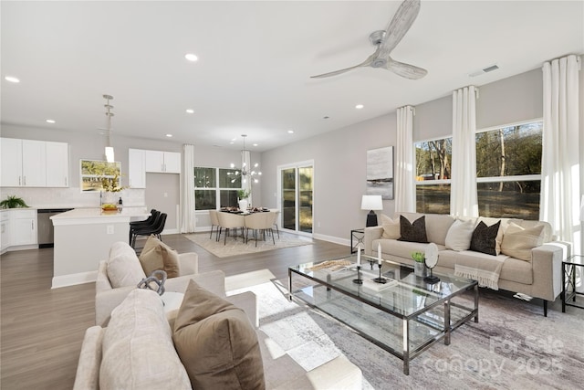 living room featuring ceiling fan with notable chandelier and light wood-type flooring