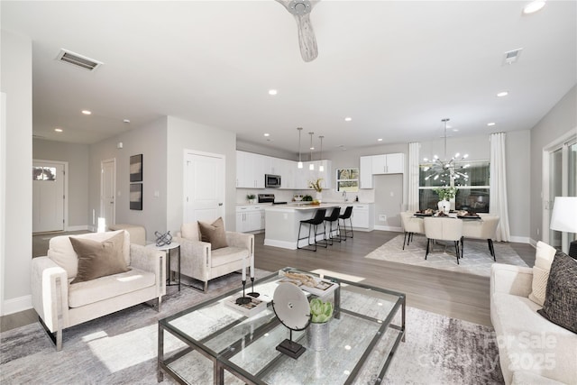 living room featuring ceiling fan with notable chandelier and light wood-type flooring