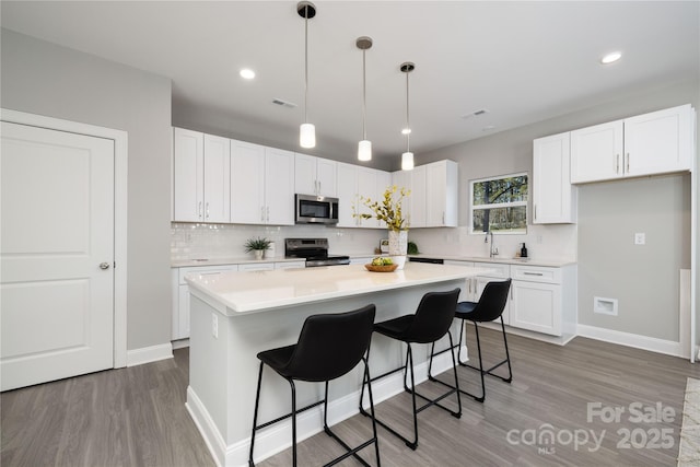 kitchen featuring a center island, tasteful backsplash, decorative light fixtures, white cabinetry, and stainless steel appliances