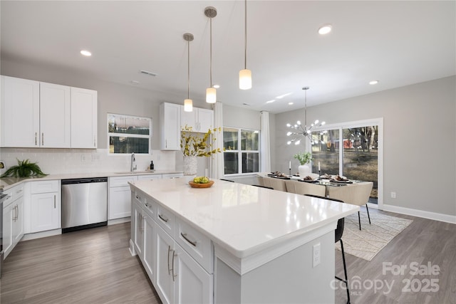 kitchen featuring stainless steel dishwasher, sink, pendant lighting, white cabinets, and a kitchen island