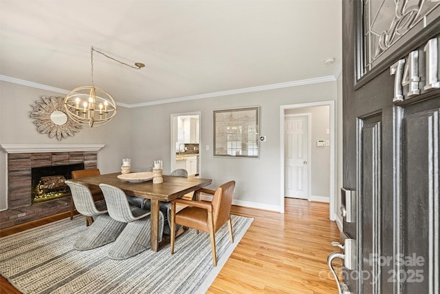 dining space with light wood-type flooring, an inviting chandelier, ornamental molding, and a tiled fireplace