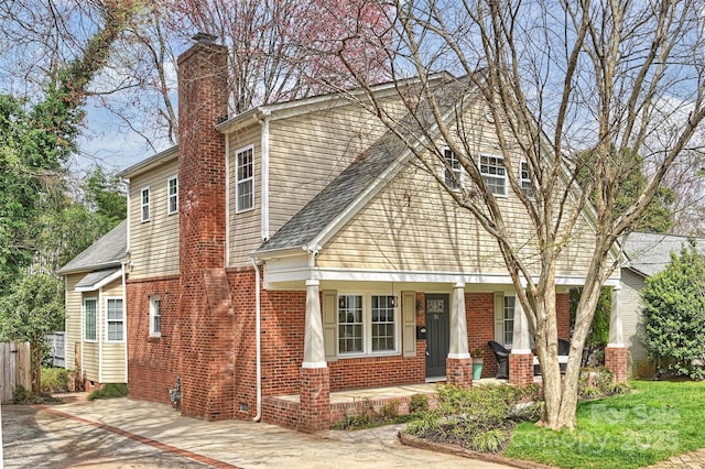 view of front of home featuring a porch, a chimney, brick siding, and fence