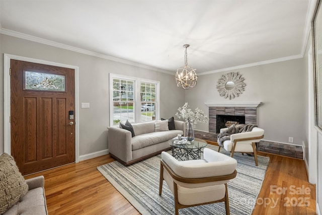 living room with a chandelier, crown molding, light wood finished floors, baseboards, and a fireplace with raised hearth