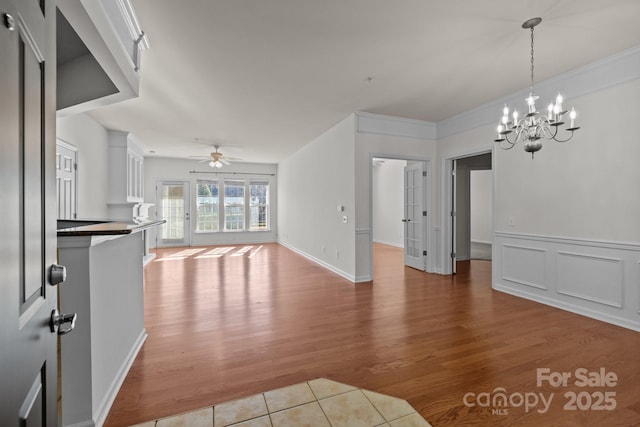 unfurnished living room with ceiling fan with notable chandelier, crown molding, and light hardwood / wood-style floors