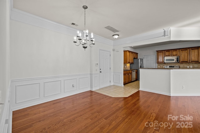 kitchen with an inviting chandelier, light hardwood / wood-style flooring, crown molding, decorative light fixtures, and appliances with stainless steel finishes