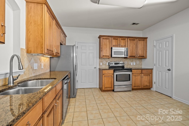 kitchen with stainless steel appliances, tasteful backsplash, dark stone counters, and sink