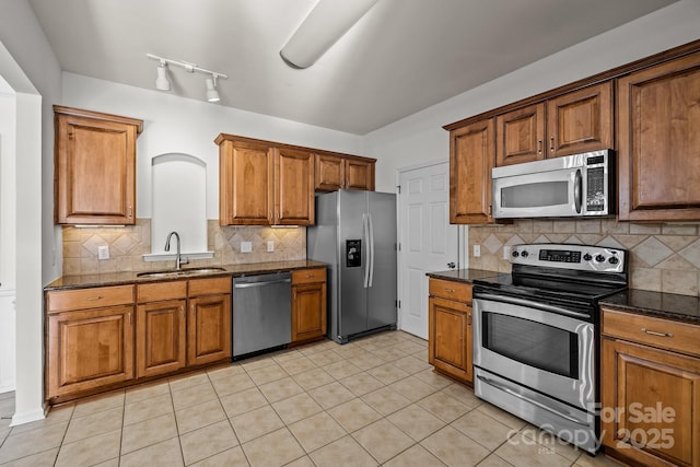 kitchen featuring backsplash, sink, dark stone countertops, light tile patterned floors, and stainless steel appliances