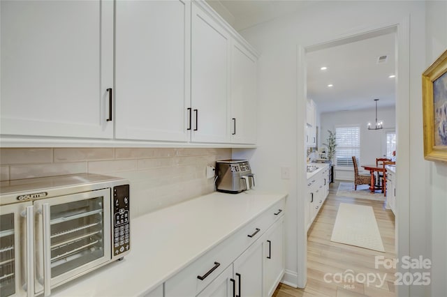 kitchen with decorative backsplash, stainless steel microwave, light countertops, light wood-style floors, and white cabinetry