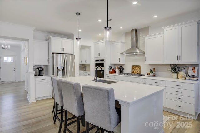 kitchen featuring stainless steel appliances, a kitchen bar, a kitchen island with sink, a sink, and wall chimney exhaust hood