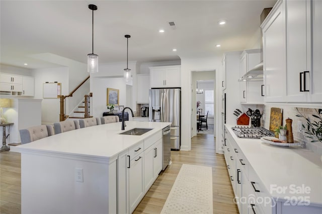 kitchen with light wood-style flooring, under cabinet range hood, stainless steel appliances, a sink, and tasteful backsplash