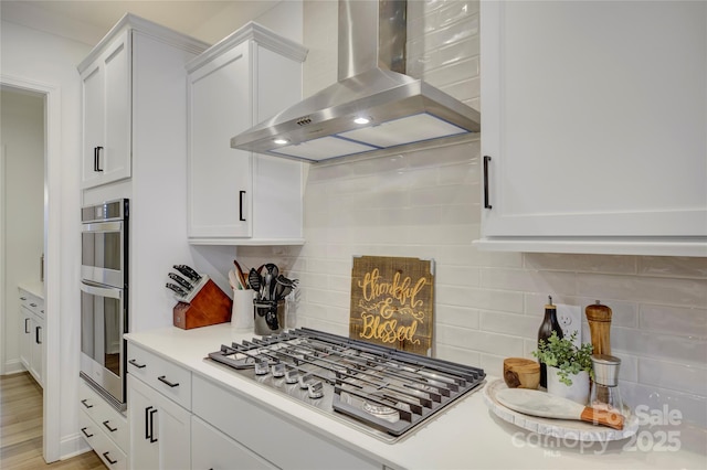 kitchen featuring wall chimney range hood, tasteful backsplash, appliances with stainless steel finishes, and white cabinets