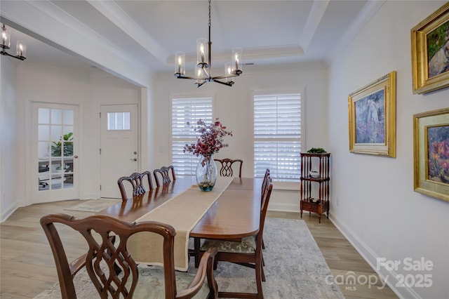 dining area featuring a notable chandelier, baseboards, ornamental molding, light wood finished floors, and a raised ceiling