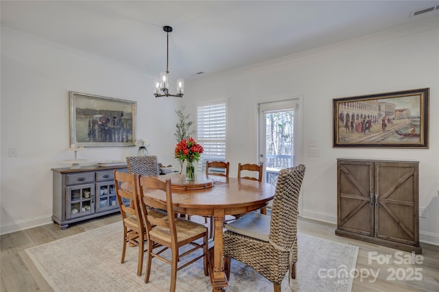 dining room featuring light wood finished floors, visible vents, baseboards, crown molding, and a notable chandelier