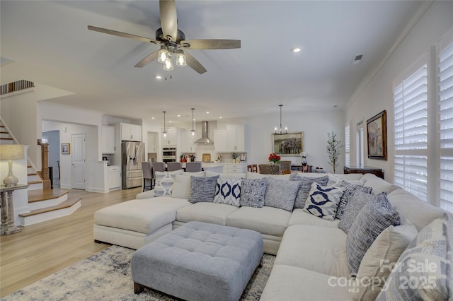 living area featuring light wood-style flooring, stairs, ceiling fan with notable chandelier, and recessed lighting