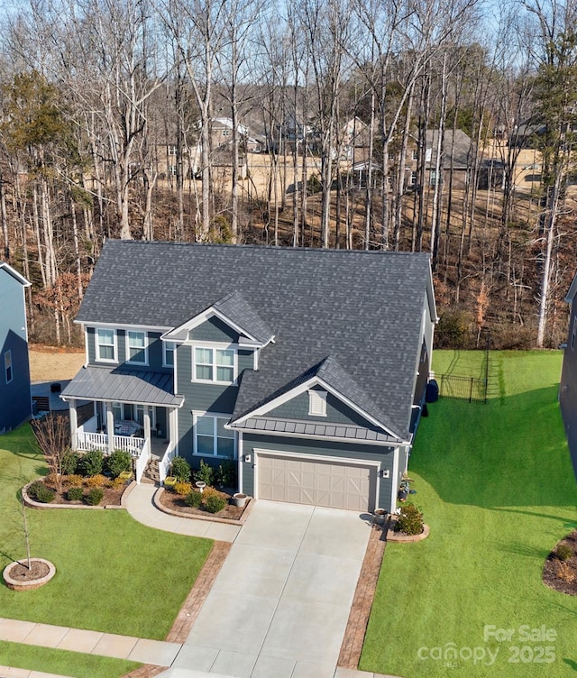 traditional home with covered porch, a garage, driveway, roof with shingles, and a front yard