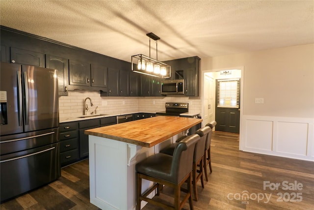 kitchen with butcher block counters, sink, decorative light fixtures, a kitchen island, and appliances with stainless steel finishes