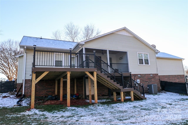 snow covered rear of property with central air condition unit, a wooden deck, and a sunroom