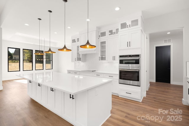 kitchen featuring stainless steel double oven, white cabinetry, a center island, and pendant lighting