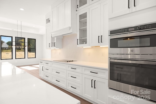 kitchen featuring hanging light fixtures, black electric cooktop, tasteful backsplash, white cabinetry, and stainless steel double oven