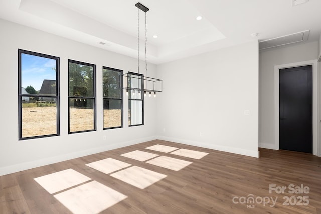 unfurnished dining area with a raised ceiling, hardwood / wood-style floors, and a notable chandelier