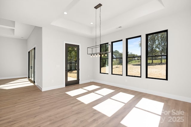 interior space with an inviting chandelier, light hardwood / wood-style floors, and a raised ceiling