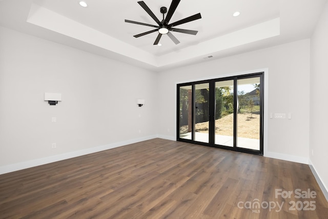 spare room with ceiling fan, dark hardwood / wood-style floors, and a tray ceiling