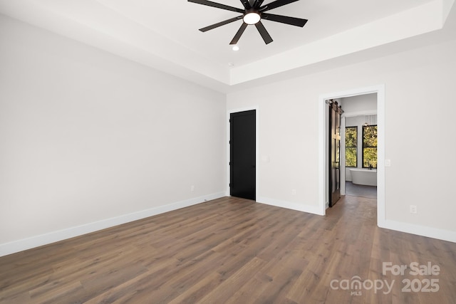 empty room with a tray ceiling, ceiling fan, and dark wood-type flooring