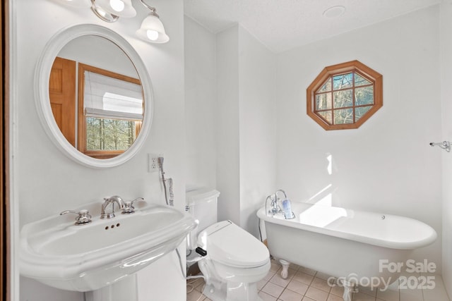 bathroom with a freestanding bath, toilet, a sink, a textured ceiling, and tile patterned flooring