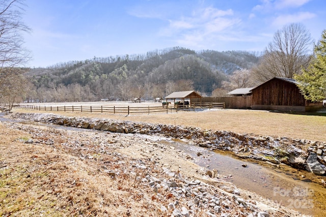 view of yard featuring a barn, a forest view, a rural view, fence, and an outdoor structure