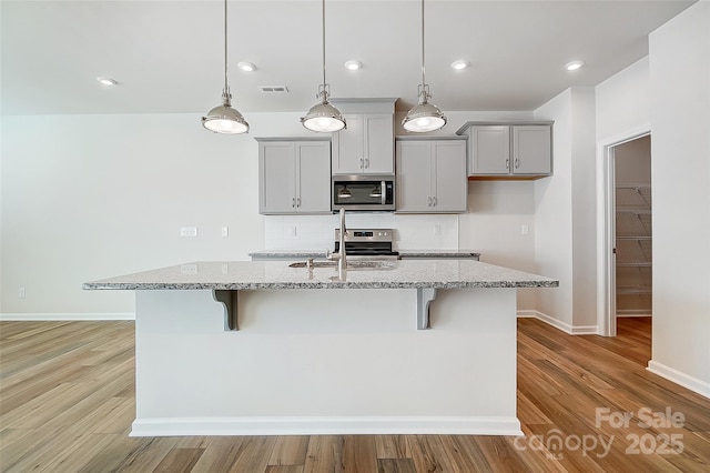 kitchen with light stone countertops, a center island with sink, and appliances with stainless steel finishes