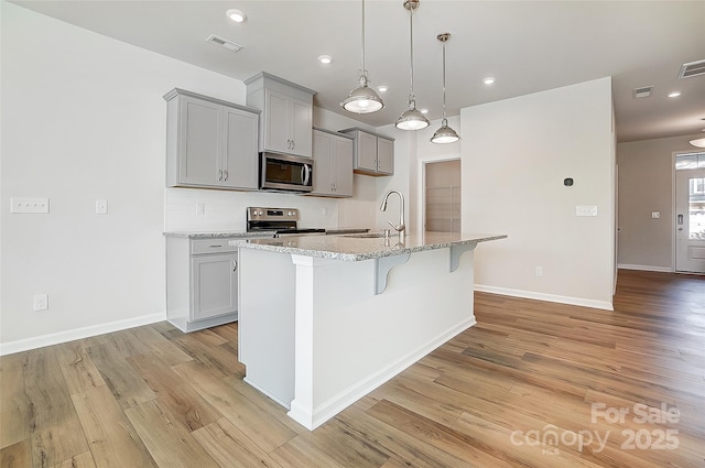 kitchen with light stone countertops, sink, hanging light fixtures, stainless steel appliances, and a kitchen island with sink