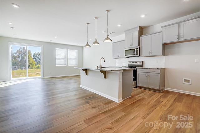 kitchen with pendant lighting, a kitchen island with sink, gray cabinets, light wood-type flooring, and stainless steel appliances