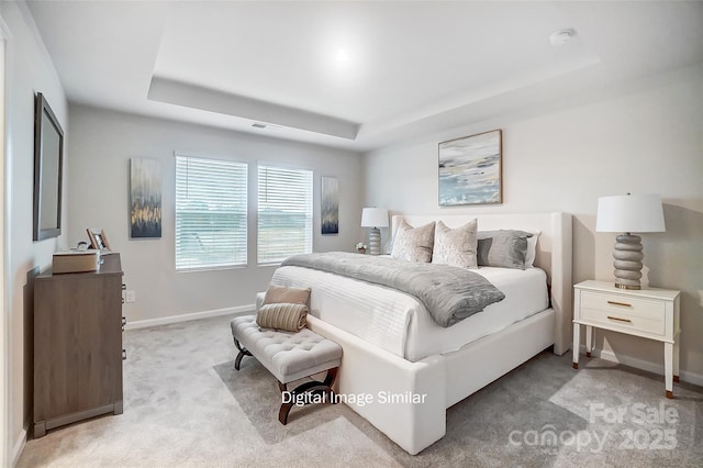 bedroom with a raised ceiling and light colored carpet