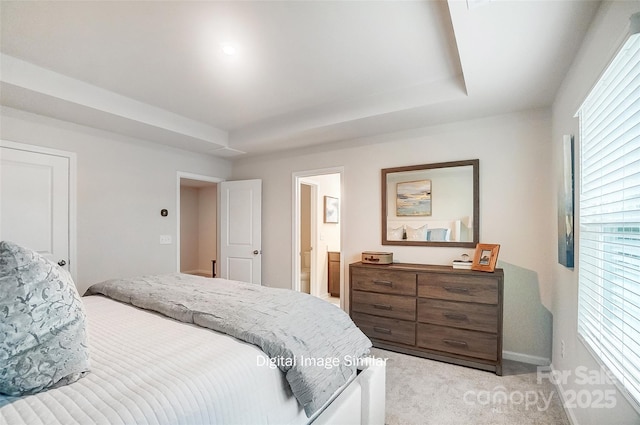 bedroom with a raised ceiling, light colored carpet, and ensuite bath