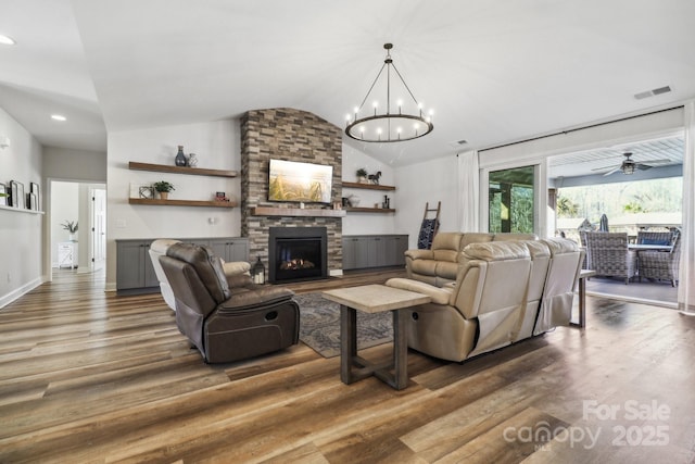 living room with ceiling fan with notable chandelier, dark hardwood / wood-style flooring, a stone fireplace, and lofted ceiling