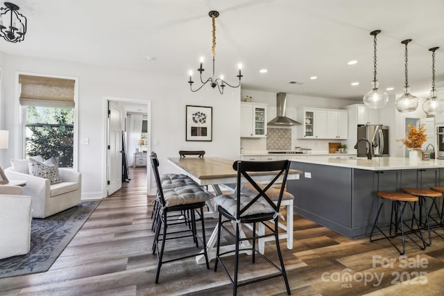 kitchen with wall chimney range hood, white cabinets, dark hardwood / wood-style floors, hanging light fixtures, and a breakfast bar area