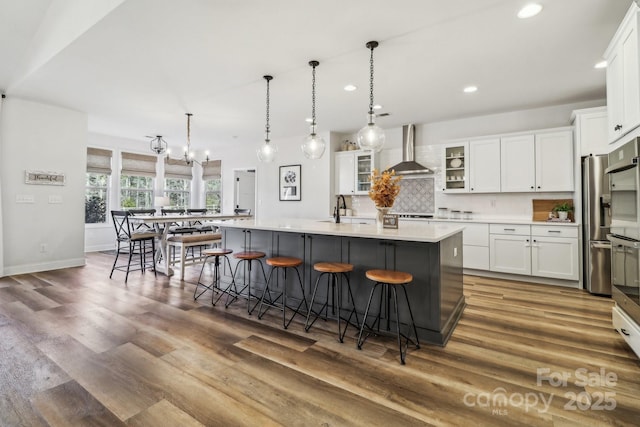 kitchen featuring wall chimney exhaust hood, a breakfast bar, sink, a large island with sink, and white cabinetry