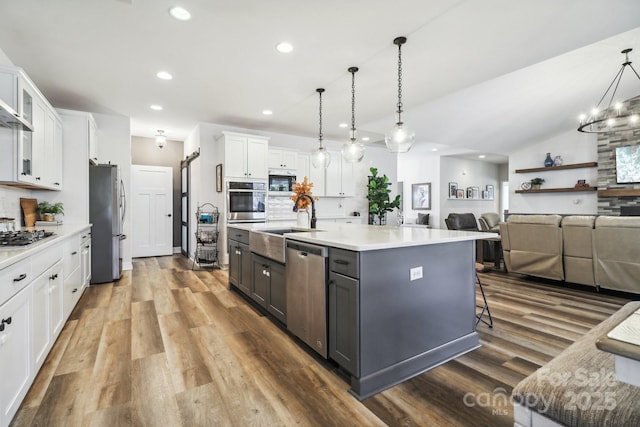 kitchen with a center island with sink, hanging light fixtures, tasteful backsplash, white cabinetry, and stainless steel appliances