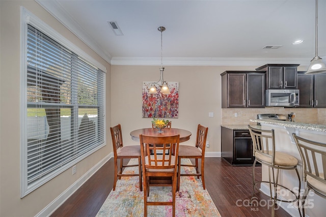 dining area with dark wood-type flooring, ornamental molding, and a chandelier