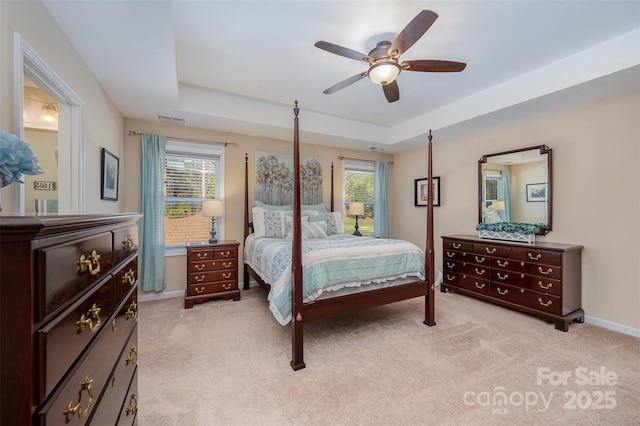 bedroom featuring light carpet, ceiling fan, and a tray ceiling