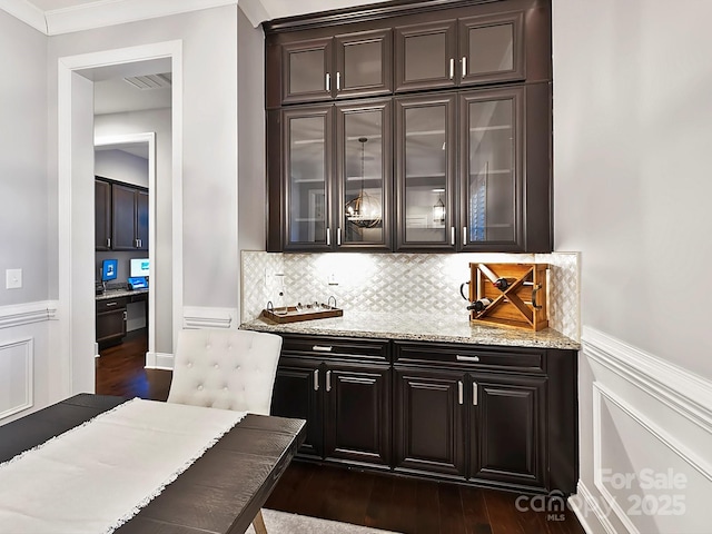 bar with crown molding, light stone countertops, dark hardwood / wood-style floors, dark brown cabinets, and tasteful backsplash