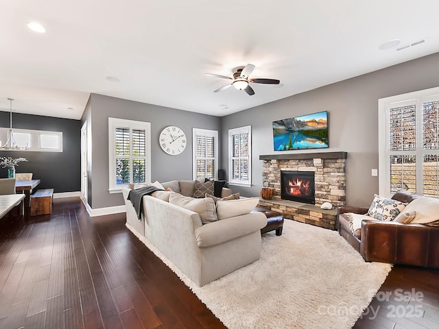 living room featuring a stone fireplace, ceiling fan, and dark wood-type flooring