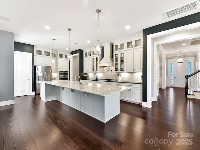 kitchen featuring a large island, appliances with stainless steel finishes, light stone countertops, premium range hood, and white cabinetry