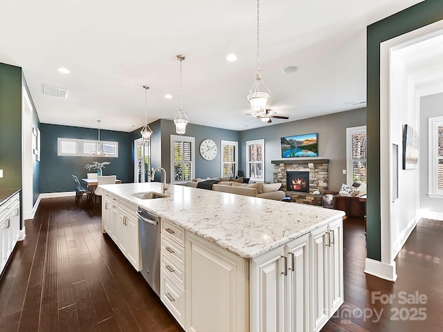 kitchen with a stone fireplace, dishwasher, a kitchen island with sink, sink, and decorative light fixtures