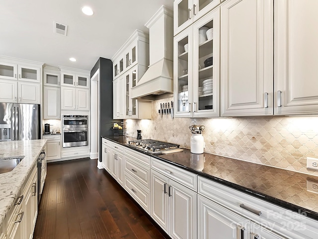 kitchen with white cabinetry, tasteful backsplash, dark stone countertops, appliances with stainless steel finishes, and custom exhaust hood