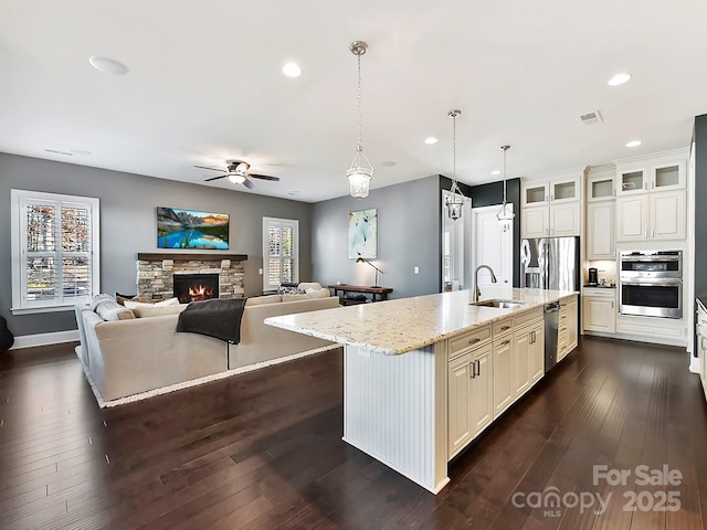 kitchen featuring appliances with stainless steel finishes, an island with sink, light stone countertops, sink, and decorative light fixtures