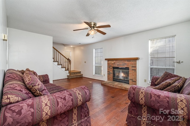 living room featuring a textured ceiling, a brick fireplace, dark hardwood / wood-style flooring, and ceiling fan