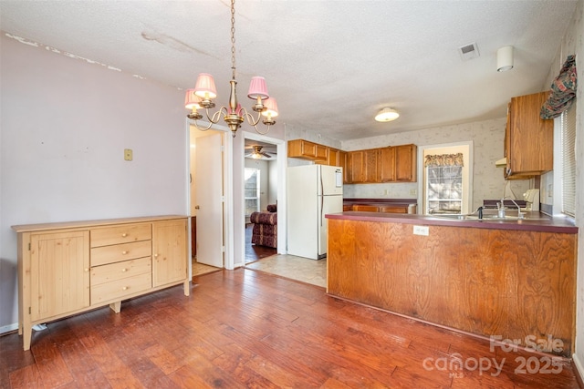 kitchen with a textured ceiling, dark wood-type flooring, white refrigerator, and hanging light fixtures