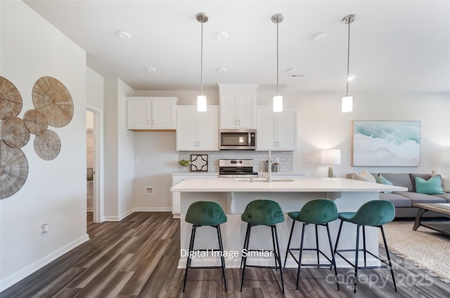 kitchen with a kitchen island with sink, white cabinets, hanging light fixtures, decorative backsplash, and stainless steel appliances